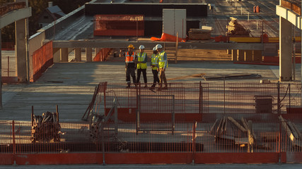 Aerial View: Diverse Team of Specialists Talking On the Roof Commercial, Industrial Building / Skyscraper Formwork Construction Site. Real Estate Project Civil Engineer, Investor, Architect and Worker