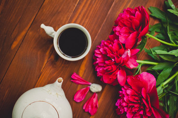 a cup of coffee and a bouquet of red peonies on a wooden table