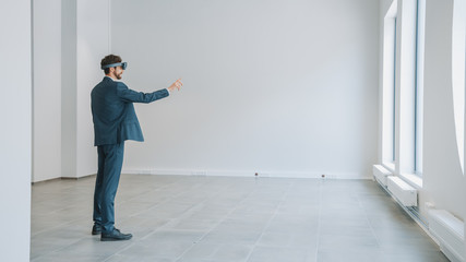 Businessman in Holographic Augmented Reality Glasses Standing in Empty Office and Map it. Sunlight Shines Through Big Windows.