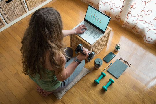 Woman working out at home on laptop while doing gymnastics. Telecommuting