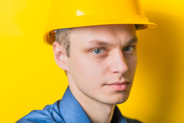 Young man close-up in yellow construction helmet and a blue shirt on a yellow background looking at the camera. Mimicry. Gesture. photo Shoot