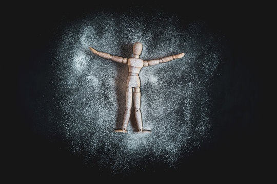 Wooden Human Manikin lying in white snow powder making snow angels with a black background
