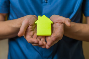 Young man holding a house made of paper. On a yellow background.
