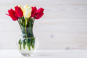 Bouquet of tulips in vase on white wooden board background. Empty place for text. Floral frame, wood backdrop. Gift card with copy space, mockup.