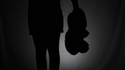 A girl with doll in the dark standing and playing with it