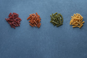 Four types of plant-based uncooked pasta made of spinach, broccoli, lentil, red bell pepper, tomato, pumpkin, butternut squash on grey background. Top View.