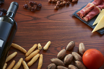 
Bottle of wine, ham, cheese, bread, raisins, tomato, hazelnut and olive oil on a wooden background. The image contains space for a text.
