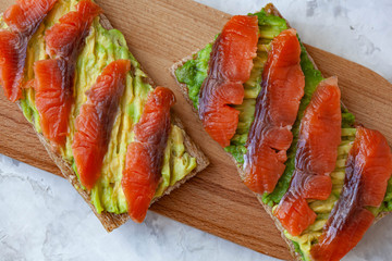 Two sandwiches with red fish and avocado on wooden cutting board
