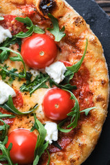 Homemade pizza with mozzarella, parmesan, chorizo and arugula on a dark background. Close-up top view.