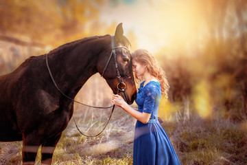 A beautiful girl with her wavy hair in a blue dress is pressed against the horse's head. A bay...