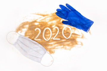 Sand on a white background. The inscription 2020 on the hub, a protective mask around the sand and blue gloves.  Summer in Covi-19. A vision of summer in 2020 during the Coronavirus pandemic.