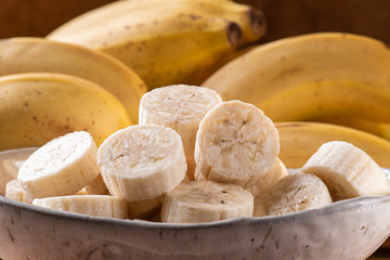 
Bananas cut in a bowl with some bananas in the background