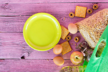 A green grocery bag on a pink wooden table. The concept of food delivery. green empty plate.