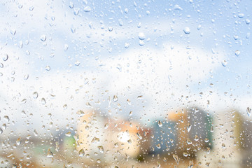 Raindrops on window glass against blue sky with white clouds