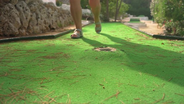 Older woman playing minigolf, closeup on her feet in sandals, blue ball - she misses hole many times