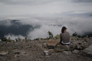 woman is siiting on top of montain, among clouds, sky scenery
