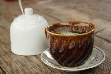 close up of brown cup of coffee with white sugar bowl on wooden table