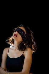 Portrait of beautiful young woman tying her eyes with black scarf on black background
