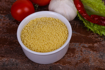 Raw couscous in the bowl served salad leaves, tomato and pepper