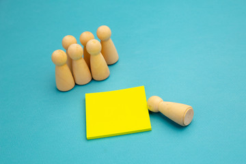 Group of people and a one separate person. Wooden pawns with yellow sticky note for writing.
