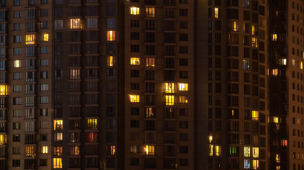 Fototapeta na wymiar Glowing apartment building windows at night. Outdoor view of living house facade with warm illumination light. Architecture, urban concept