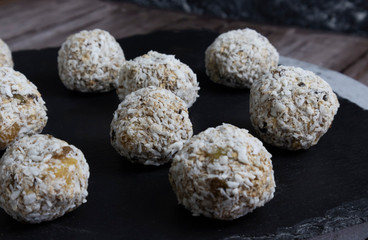 Closeup on a black plate of energy balls in coconut flakes, protein balls with dried fruits honey and bananas