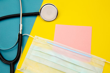 Stethoscope, face mask and pink sticky note for text on colorful background.