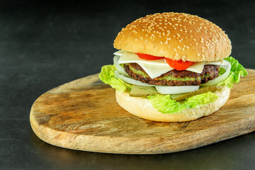 Hamburger vegetarian with spinach, lettuce, onion, tomatoes and cheese on the wooden cutting board isolated. Delicious burger of spinach for vegetarians.