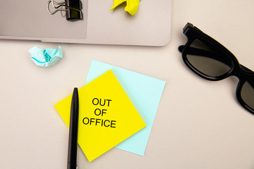 Out of office, message on pink sticky note. Workspace with laptop, glasses and pen. Work from home...