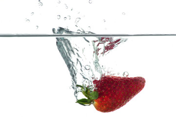 A high speed photograph of a single strawberry falling into a transparent basin of water.