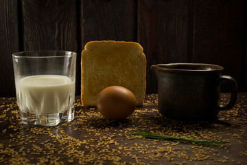 country breakfast of bread, egg and milk on a background of seeds, a saucepan and wood
