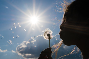 girl blowing dandelion against the light