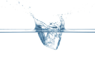 An ice cube falling into a transparent water basin over a white background.