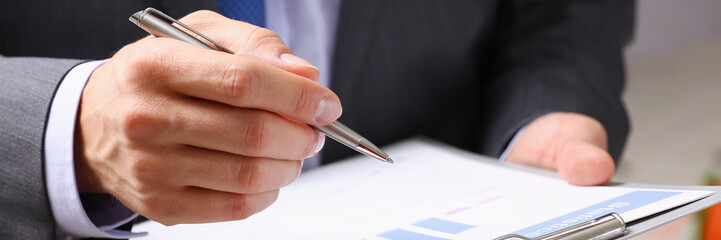 Hand of businessman in suit filling and signing with silver pen partnership agreement form clipped to pad closeup. Management training course, some important document, team leader ambition concept