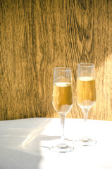 Two glasses of champagne. Glass goblets with alcohol on background of wooden wall. White linen tablecloth. Selective focus image. Copy space.