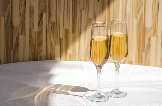 Two glasses of champagne. Glass goblets with alcohol on background of wooden wall. White linen tablecloth. Selective focus image. Copy space.