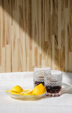Top view. Flat lay. Two crystal glasses of whiskey. Glass goblets with alcohol on background of wooden wall.Saucer with sliced yellow lemon. Direct sunlight, long shadows. Selective focus image.