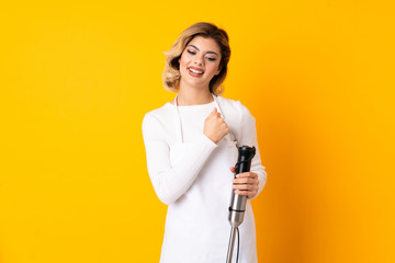 Girl using hand blender isolated on yellow background celebrating a victory