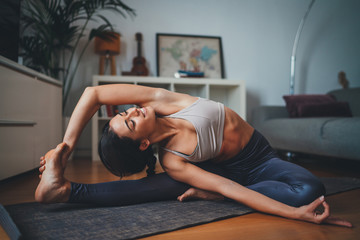 Young healthy beautiful woman in sportive top and leggings practicing yoga at home stretching body...