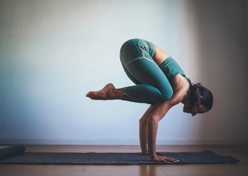 Young sportive woman practicing yoga in the morning at home making Crow Pose, Yoga Full Body Home Workout, blank space for text message or content