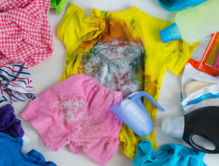 Dirty kids clothing is scattered on a white wooden table.Concept of searching for information on washing spots, the best means for cleaning clothes.banner to promote advertising, sales.