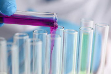 A male chemist holds test tube of glass in his hand overflows a liquid solution of potassium permanganate conducts an analysis reaction takes various versions of reagents using chemical manufacturing