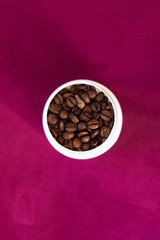 Coffee roasted brown beans in a white Cup on a purple background