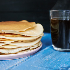 A stack of pancakes on a plate of black coffee on a blue wooden table