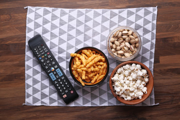A bowl of popcorn chips, nut and TV remote,