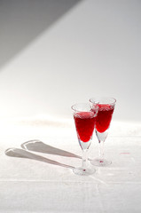 Two crystal glasses with red wine. Glass goblets with alcohol on background of wooden wall. White linen tablecloth. Direct sunlight, long shadows. Selective focus image. Copy space.