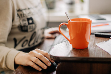 selective focus: young woman working in an online call center arranged in her room by the window. Home environment, she drinks coffee and simultaneously works on computer