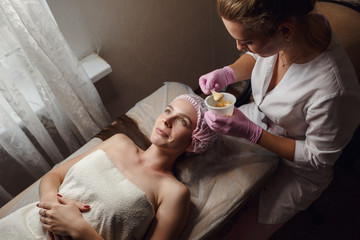 Obraz na płótnie Canvas cosmetology specialist applying gold facial mask using brush