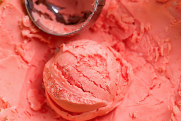 Ball of homemade natural fresh berries ice-cream coral coloured and metallic scoop on a background frome the same dessert.