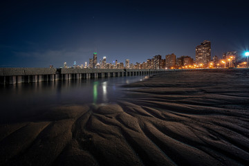 Incredible interesting and beautiful Chicago cityscape skyline at night with gorgeous foreground meandering patterns of ridges and gullies carved in sand of beach due to erosion of the receding water.